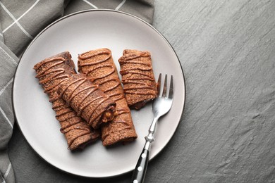 Photo of Delicious chocolate crepes with sweet paste and nuts on black table, top view. Space for text