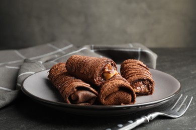 Photo of Delicious chocolate crepes with sweet paste and nuts on black table, closeup