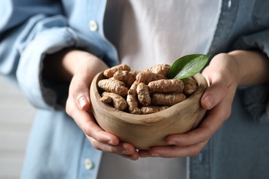 Photo of Woman holding bowl with raw turmeric roots, closeup