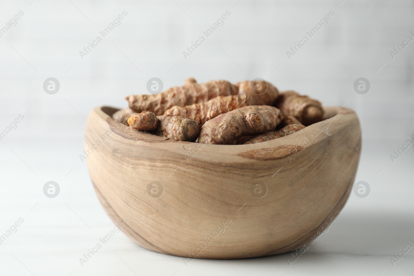 Photo of Raw turmeric roots in bowl on white marble table, closeup