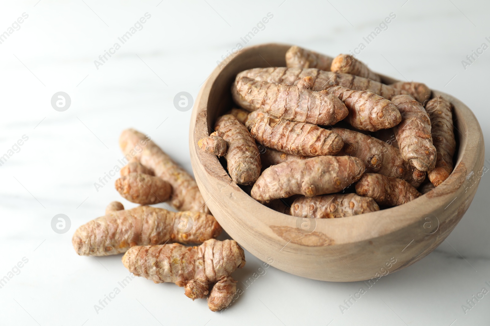 Photo of Raw turmeric roots in bowl on white marble table, closeup