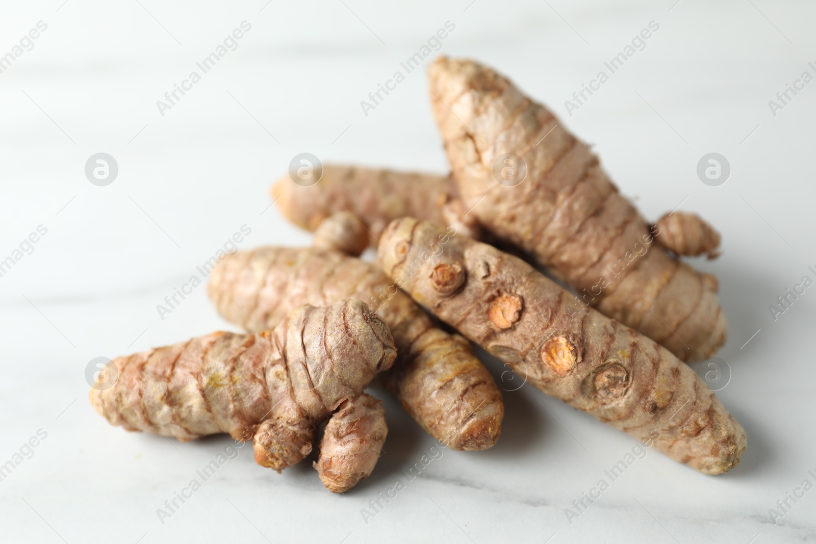 Photo of Pile of raw turmeric roots on white marble table, closeup