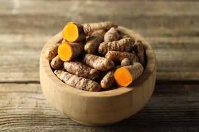 Photo of Tumeric rhizomes in bowl on wooden table, closeup