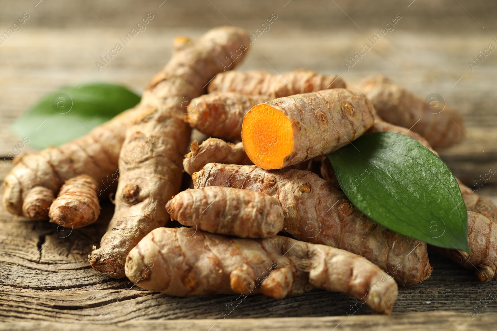 Photo of Pile of tumeric rhizomes with leaves on wooden table, closeup