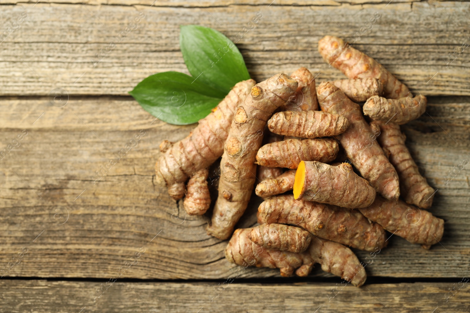 Photo of Pile of tumeric rhizomes with leaves on wooden table, top view. Space for text