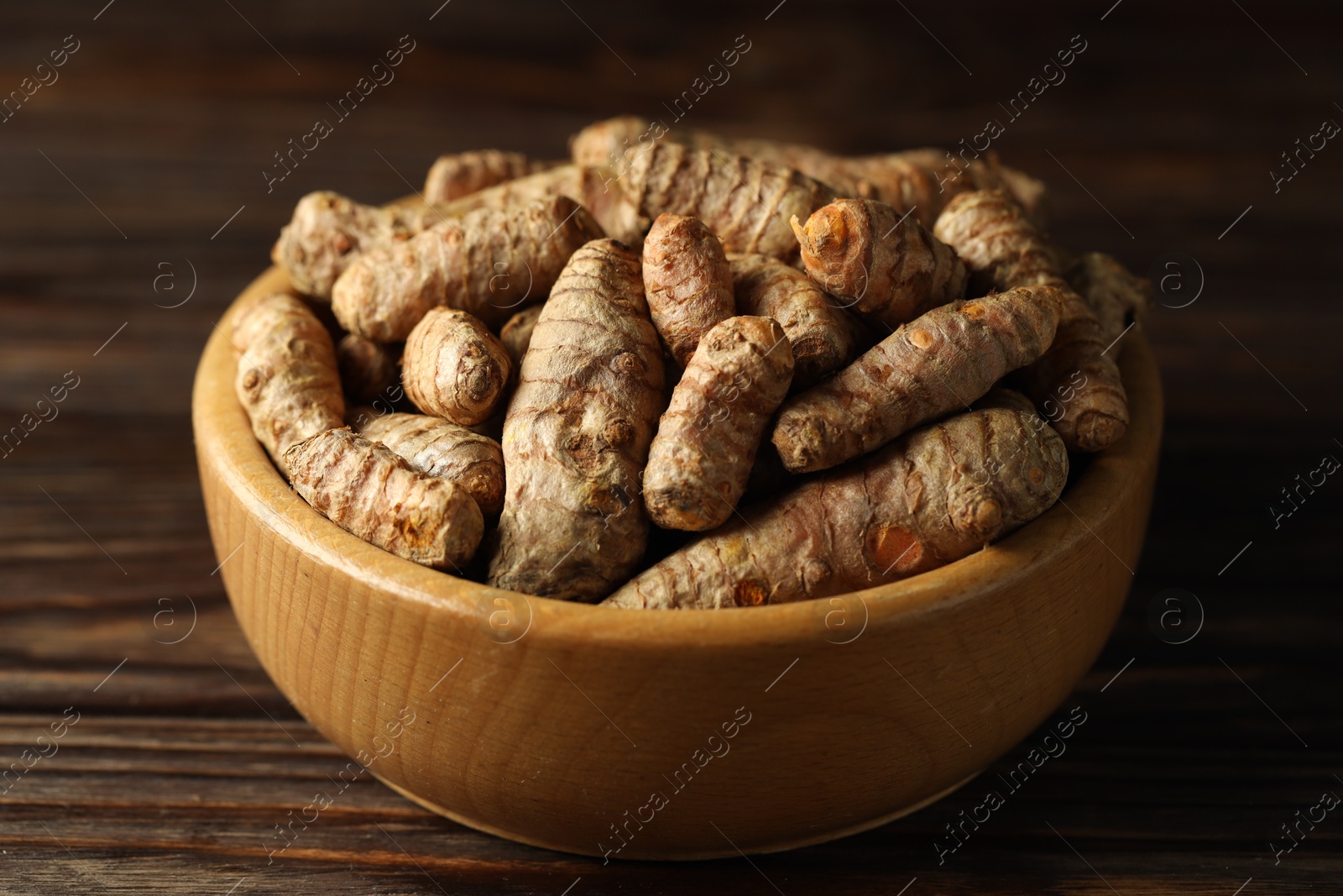 Photo of Tumeric rhizomes in bowl on wooden table, closeup