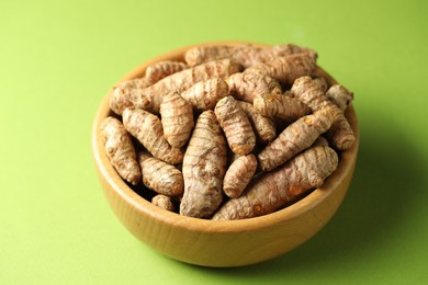 Photo of Tumeric rhizomes in bowl on green background, closeup