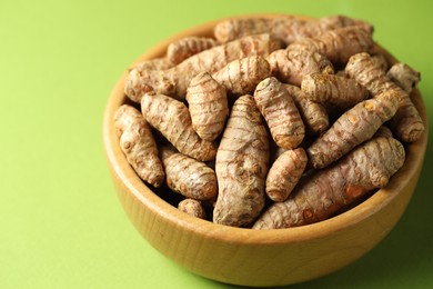 Photo of Tumeric rhizomes in bowl on green background, closeup