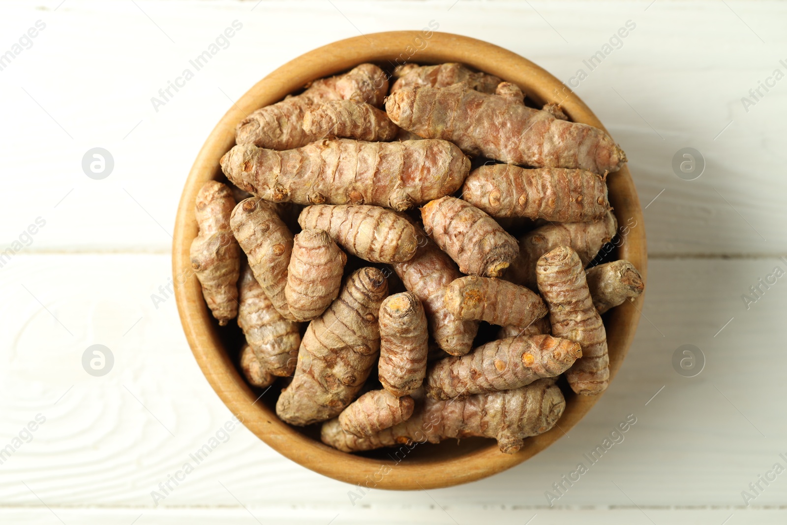 Photo of Tumeric rhizomes in bowl on white wooden table, top view