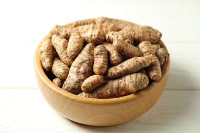 Photo of Tumeric rhizomes in bowl on white wooden table, closeup