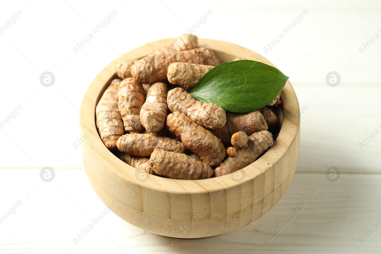 Photo of Tumeric rhizomes with leaf in bowl on white wooden table, closeup