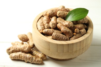 Photo of Tumeric rhizomes with leaf in bowl on white wooden table, closeup