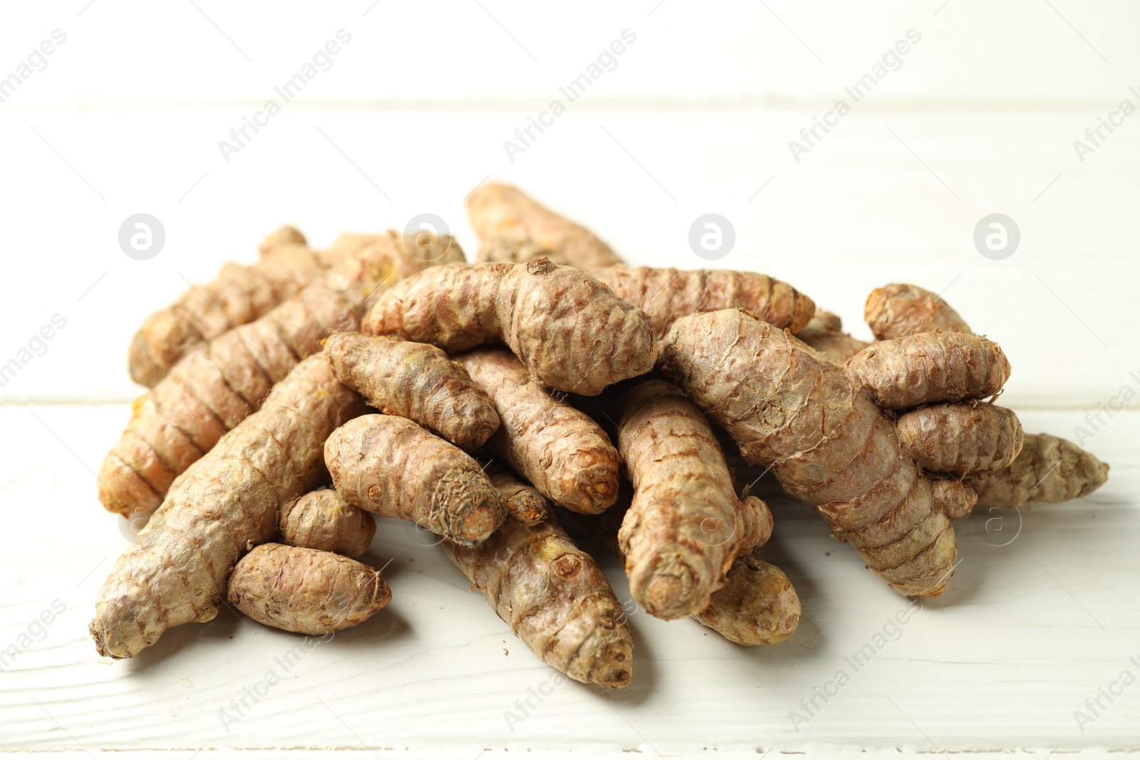 Photo of Pile of tumeric rhizomes on white wooden table, closeup