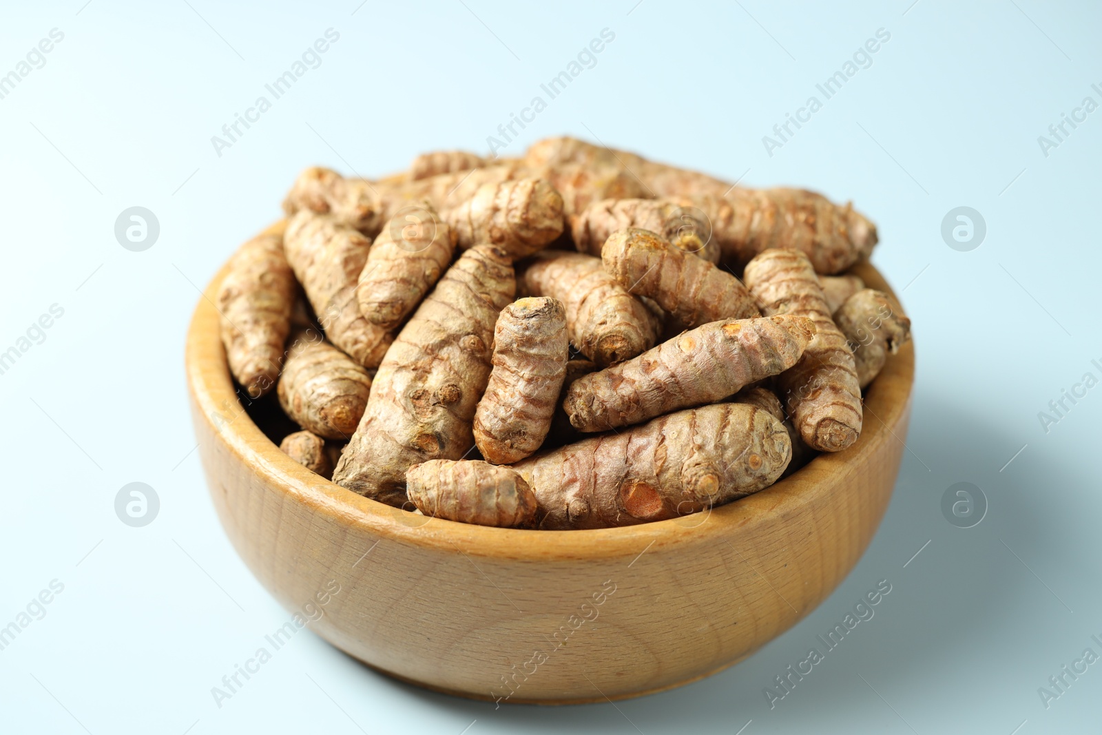 Photo of Tumeric rhizomes in bowl on light blue background, closeup