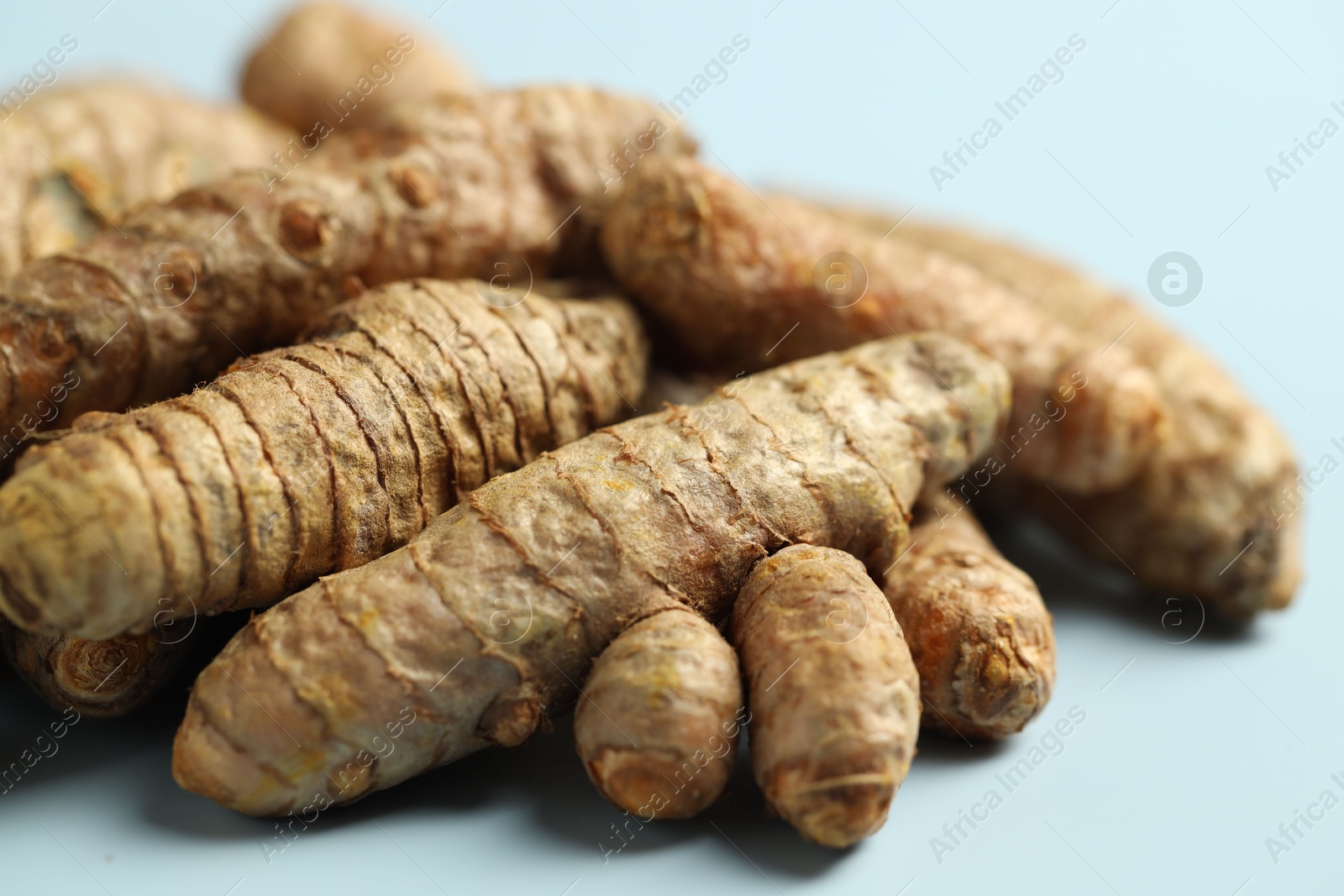 Photo of Pile of tumeric rhizomes on light blue background, closeup