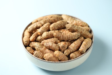 Photo of Tumeric rhizomes in bowl on light blue background, closeup