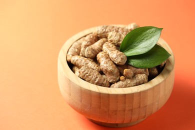 Photo of Tumeric rhizomes with leaves in bowl on orange background, closeup