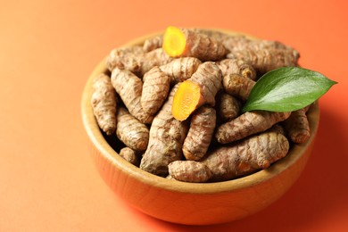 Photo of Tumeric rhizomes with leaf in bowl on orange background, closeup