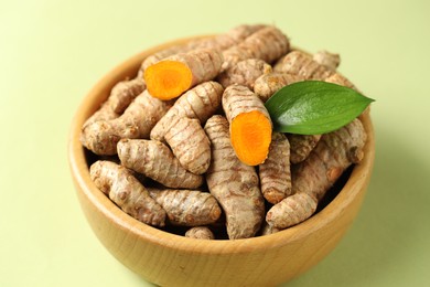 Photo of Tumeric rhizomes with leaf in bowl on light green background, closeup