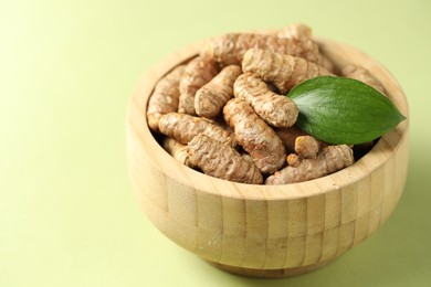 Photo of Tumeric rhizomes with leaf in bowl on light green background, closeup. Space for text