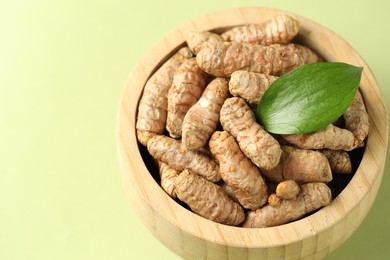 Photo of Tumeric rhizomes with leaf in bowl on light green background, closeup. Space for text