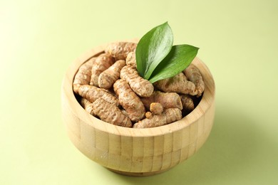 Photo of Tumeric rhizomes with leaves in bowl on light green background, closeup