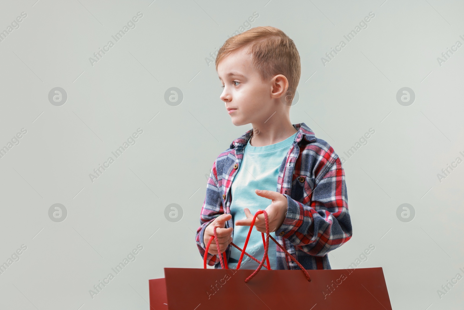 Photo of Cute little boy with shopping bags on grey background. Space for text