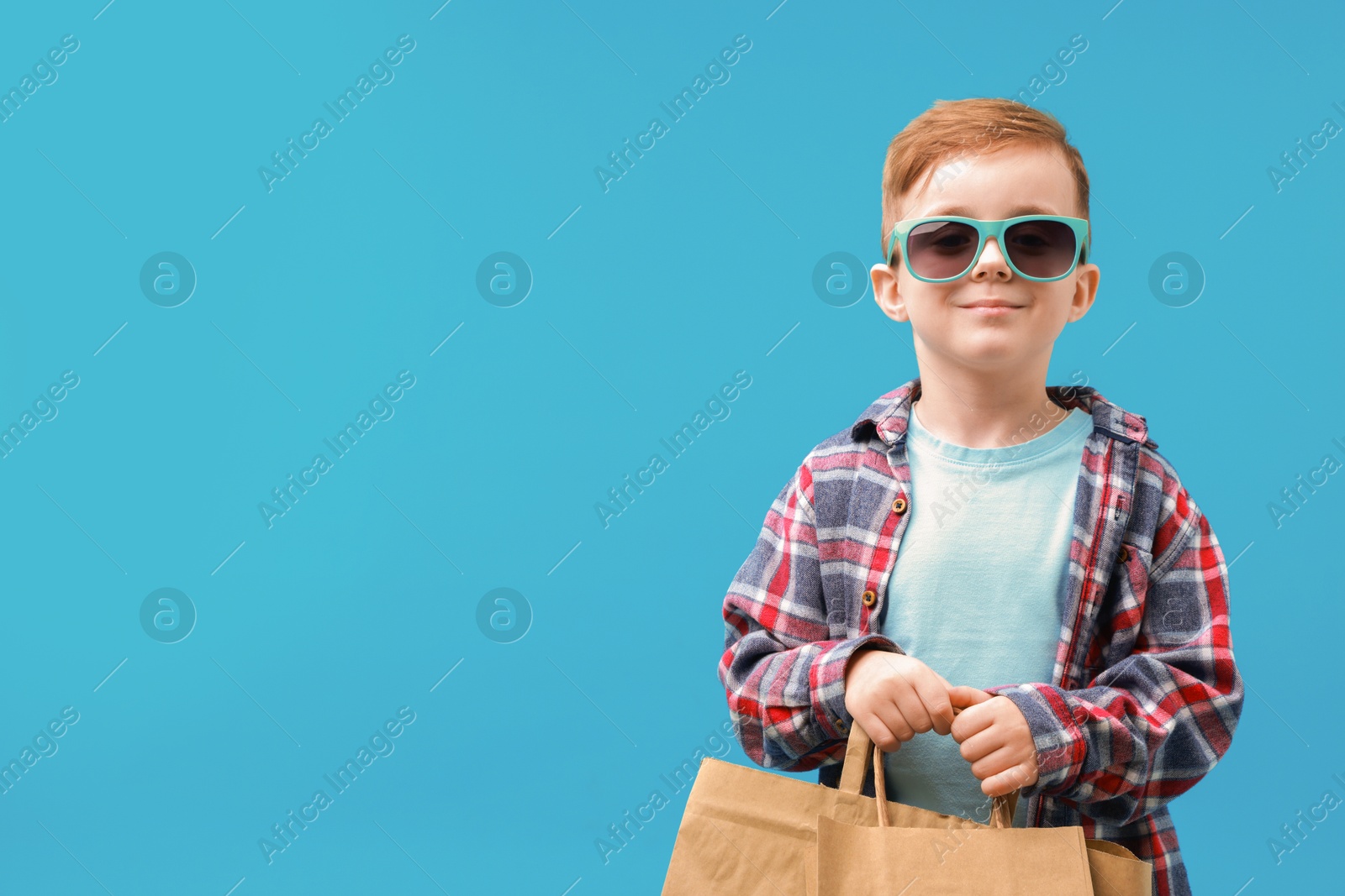 Photo of Cute little boy with shopping bags on light blue background. Space for text