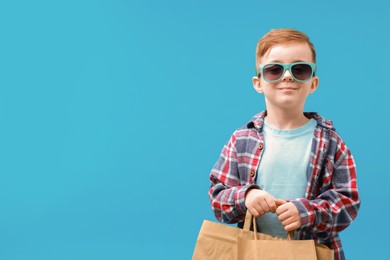 Photo of Cute little boy with shopping bags on light blue background. Space for text