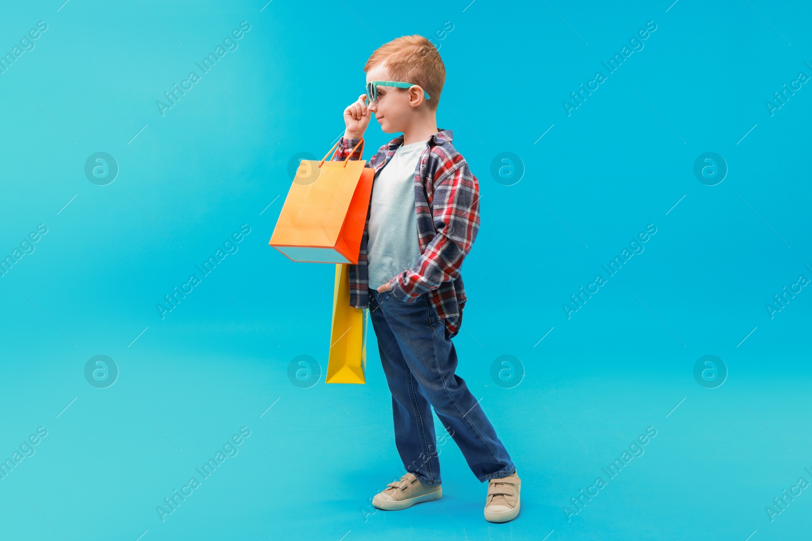 Photo of Cute little boy with shopping bags on light blue background