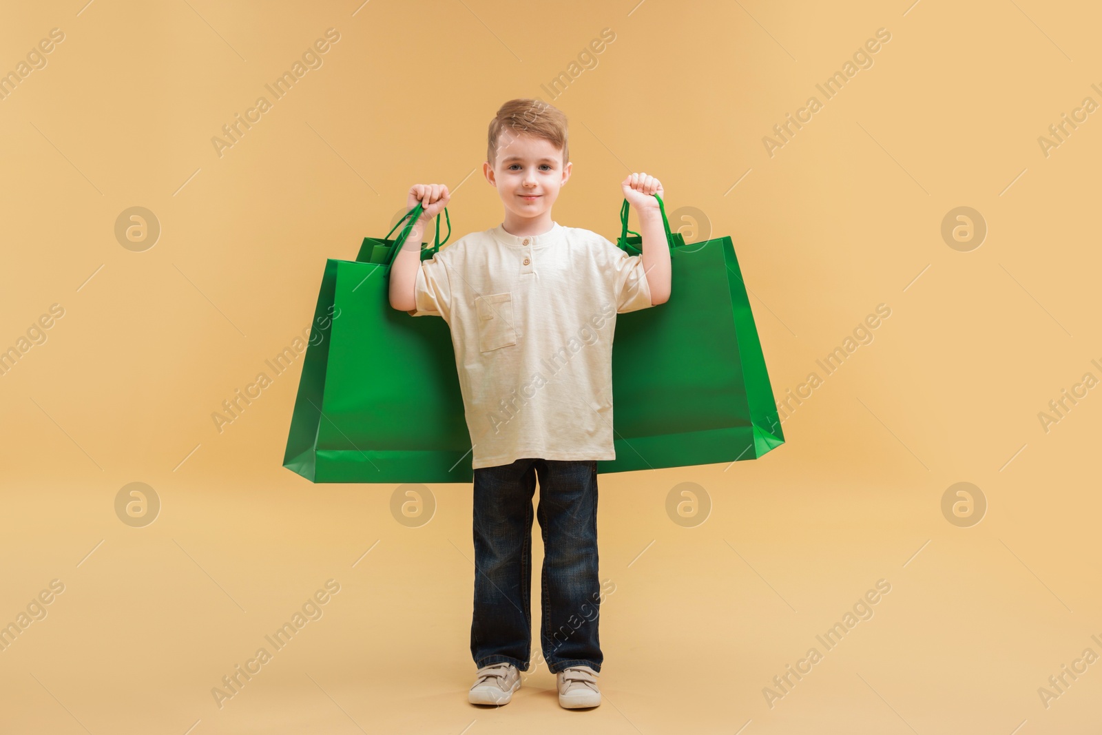 Photo of Cute little boy with shopping bags on beige background