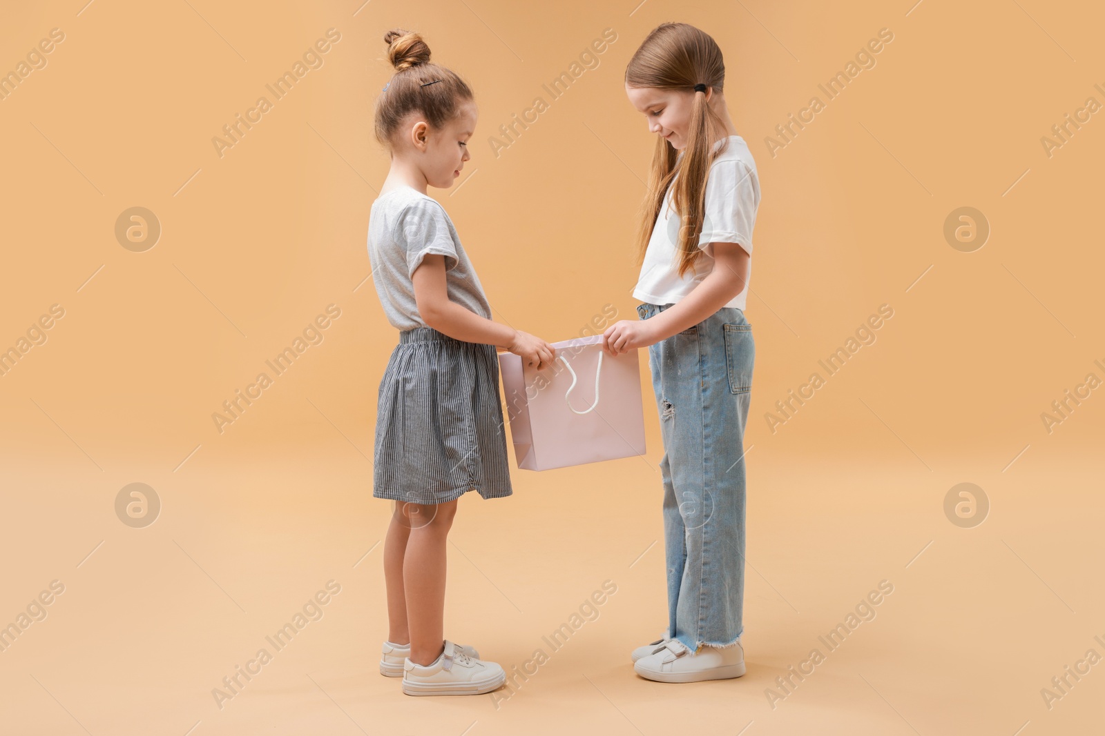 Photo of Cute little friends with shopping bag on beige background. Space for text