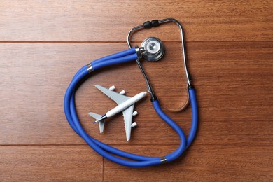 Photo of Medical tourism. Stethoscope and airplane model on wooden background, top view