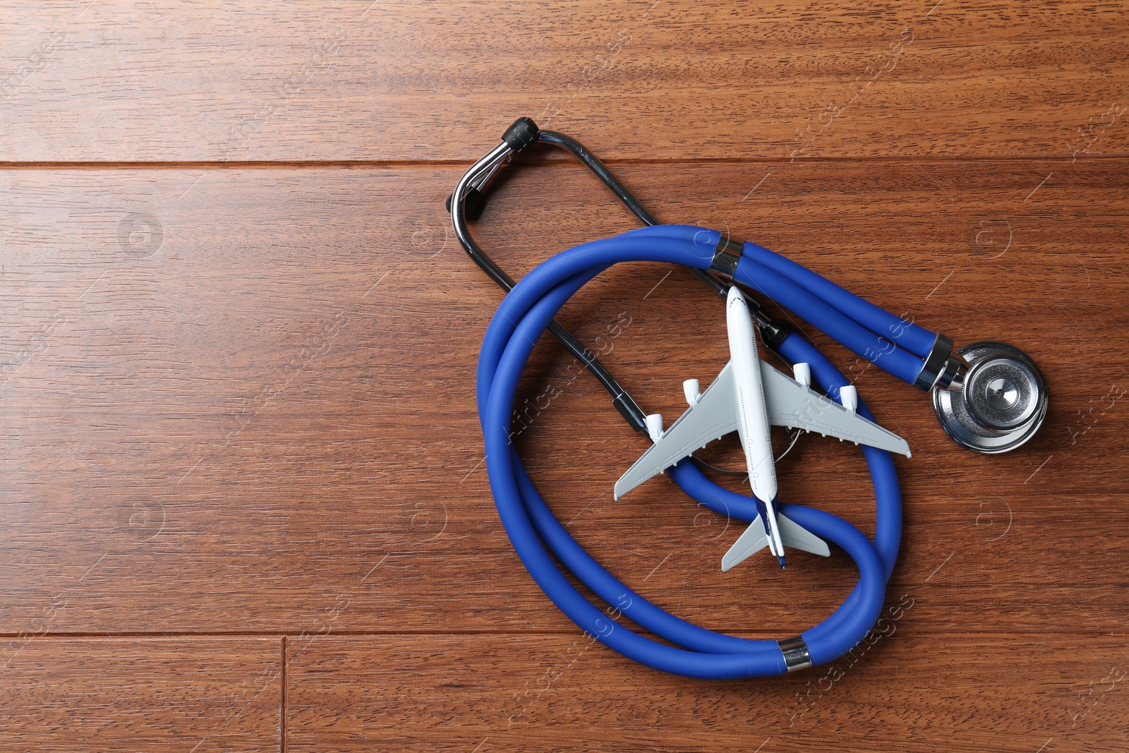 Photo of Medical tourism. Stethoscope and airplane model on wooden background, top view. Space for text