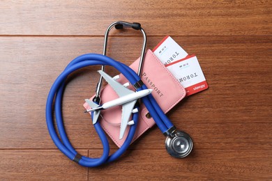 Photo of Medical tourism. Passport with tickets, stethoscope and airplane model on wooden background, top view