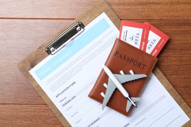 Photo of Medical tourism. Travel insurance application form, passport with tickets and airplane model on wooden background, top view