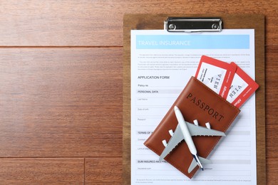 Photo of Medical tourism. Travel insurance application form, passport with tickets and airplane model on wooden background, top view. Space for text