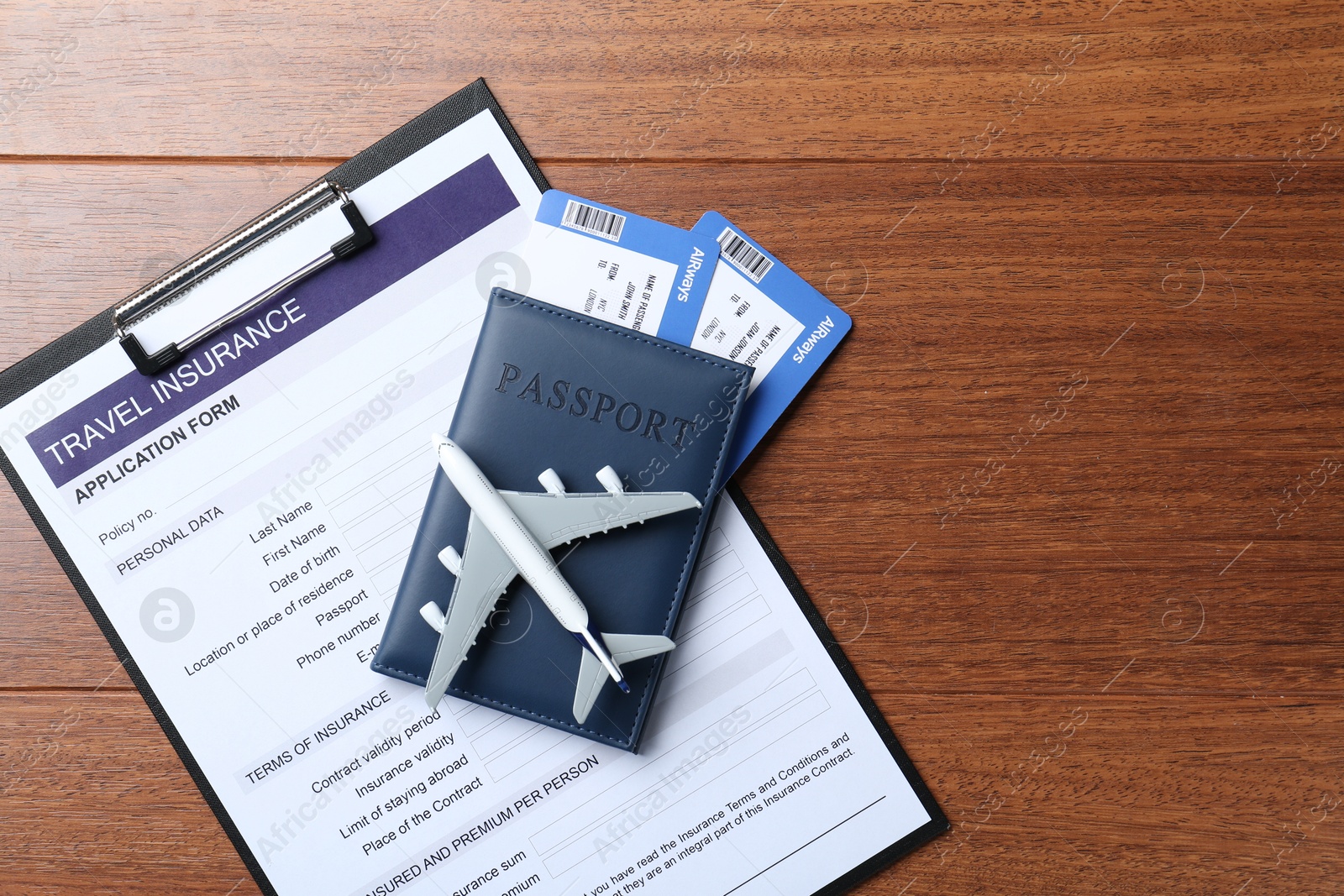 Photo of Medical tourism. Travel insurance application form, passport with tickets and airplane model on wooden background, top view. Space for text