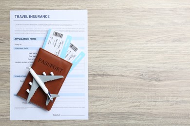 Photo of Medical tourism. Travel insurance application form, passport with tickets and airplane model on light wooden background, top view. Space for text