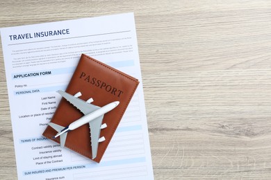 Photo of Medical tourism. Travel insurance application form, passport and airplane model on light wooden background, top view. Space for text