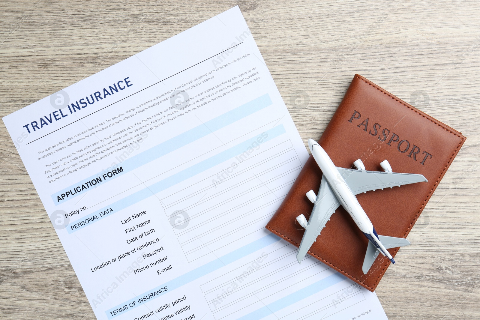 Photo of Medical tourism. Travel insurance application form, passport and airplane model on light wooden background, top view