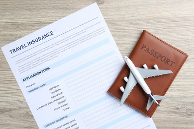 Photo of Medical tourism. Travel insurance application form, passport and airplane model on light wooden background, top view