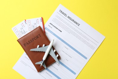 Photo of Medical tourism. Travel insurance application form, passport with tickets and airplane model on yellow background, top view