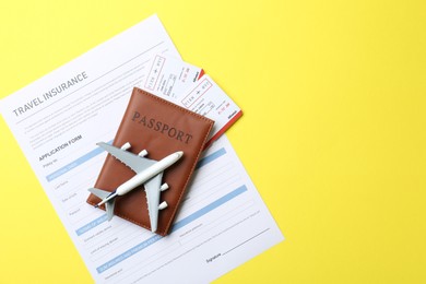 Photo of Medical tourism. Travel insurance application form, passport with tickets and airplane model on yellow background, top view. Space for text