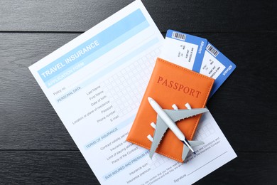 Photo of Medical tourism. Travel insurance application form, passport with tickets and airplane model on black wooden background, top view