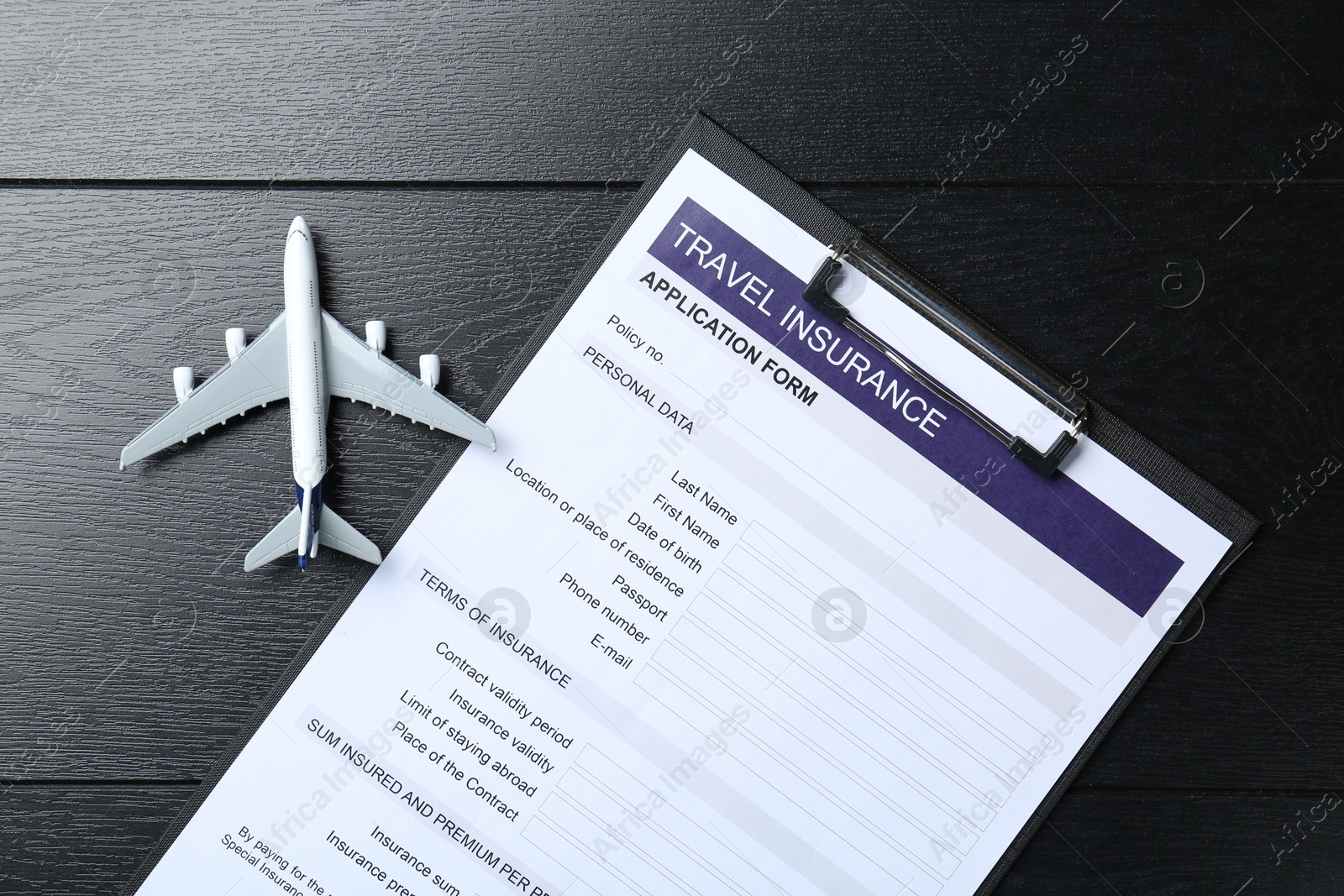 Photo of Medical tourism. Travel insurance application form and airplane model on black wooden background, top view