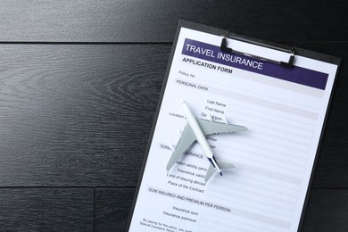 Photo of Medical tourism. Travel insurance application form and airplane model on black wooden background, top view. Space for text