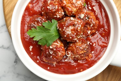 Photo of Delicious meatballs with tomato sauce, parmesan cheese and parsley served on white marble table, top view