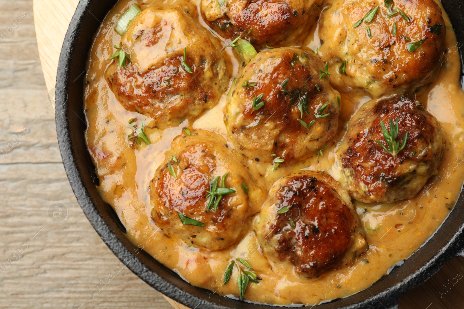 Photo of Delicious meatballs with gravy cream sauce and herbs on wooden table, top view