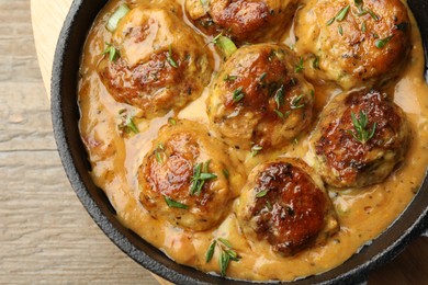 Photo of Delicious meatballs with gravy cream sauce and herbs on wooden table, top view